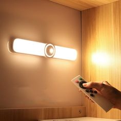 a person is holding a remote control in front of a light that is on the wall