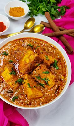 a white bowl filled with food next to bowls of spices and spoons on a table