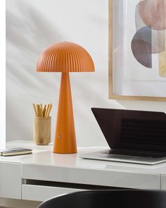 an orange table lamp sitting on top of a white desk next to a laptop computer