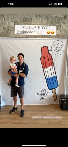 a man holding a baby standing in front of a sign