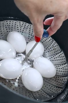 a person using a knife to cut hard boiled eggs into small balls in a colander