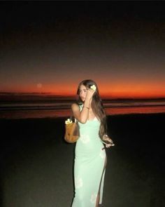 a woman in a green dress is holding a cell phone and standing on the beach