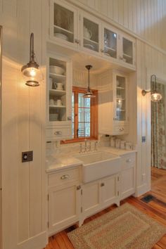 a large kitchen with white cabinets and wood flooring, along with a rug on the floor