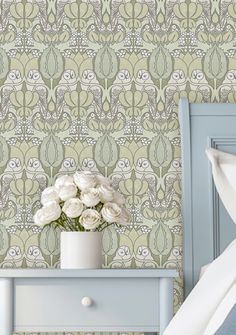 a white vase with flowers sitting on top of a blue dresser next to a bed