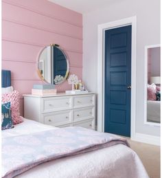 a bedroom with pink walls and blue doors, white furniture, and a bed in front of a mirror