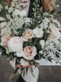 a woman holding a bouquet of white and pink flowers in her hands with greenery