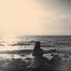 a woman sitting on rocks near the ocean