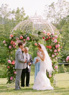 a bride and groom are standing under an arch with flowers on it, surrounded by greenery