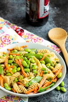 a white bowl filled with pasta and peas next to a bottle of beer on a table