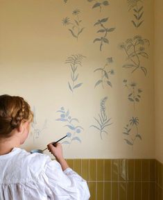 a woman painting a wall with flowers on it