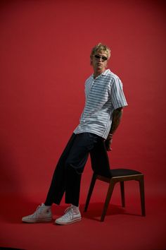 a man sitting on top of a wooden chair in front of a red wall wearing sunglasses