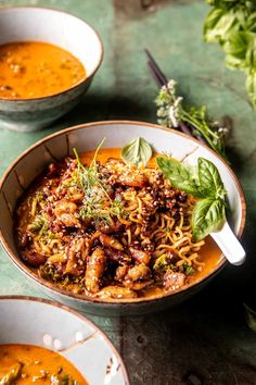 two bowls filled with noodles and meat on top of a green tablecloth next to silver spoons