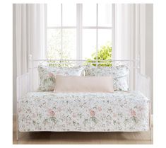 a white day bed with pink and green floral print on it, in front of a window