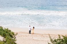 two people standing on the beach holding hands