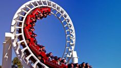 the roller coaster is red and white with people riding it on it's side