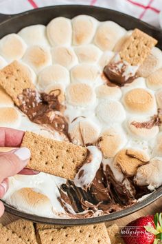 someone dipping marshmallows into a skillet with chocolate and graham crackers