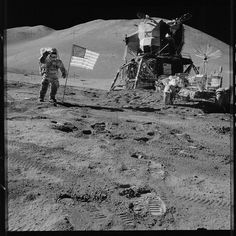 an astronaut standing on the moon next to a flag and rover vehicle with two men in space suits