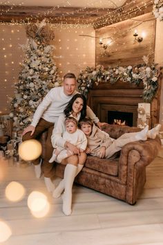 a family sitting on a couch in front of a christmas tree with lights around it