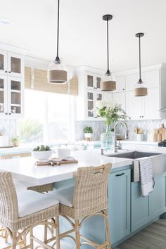 a kitchen with blue cabinets and white counter tops, an island in the middle is flanked by wicker bar stools