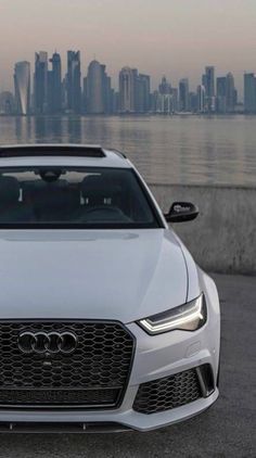 an audi car parked in front of the water with a cityscape in the background