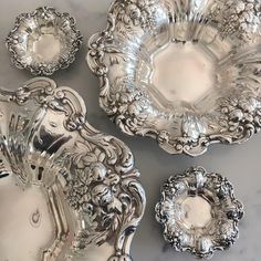 four silver plates with ornate designs on them sitting on a marble counter top, one is empty and the other two are empty