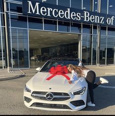 a woman leaning on the hood of a white car with a red ribbon tied around it