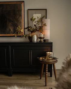 a living room with a black cabinet and gold accents on the sideboard, two candles in front of a painting