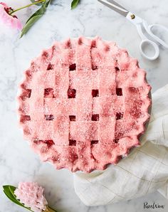 a strawberry pie with powdered sugar on top and pink flowers in the back ground