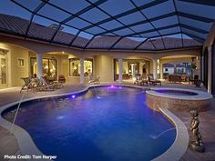 an indoor swimming pool surrounded by lounge chairs and tables at night with the lights on