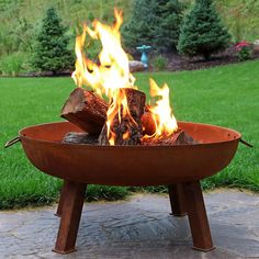 a fire pit sitting on top of a stone floor next to green grass and trees