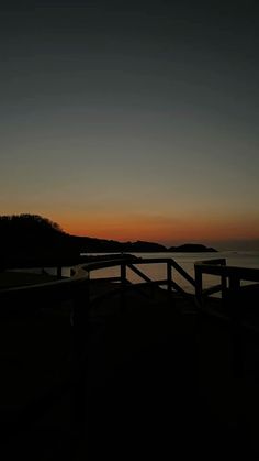 the sun is setting over the water and there are two benches on the shore line