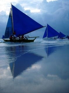 several sailboats are on the water with clouds in the sky behind them and one is blue