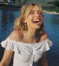 a woman is laughing while standing in front of the water with her eyes closed and mouth wide open