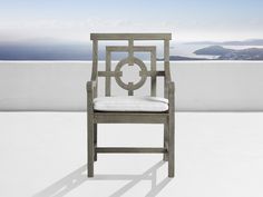 a wooden chair sitting on top of a white floor next to an ocean and sky