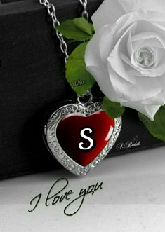 a white rose sitting next to a heart shaped necklace with the letter s on it