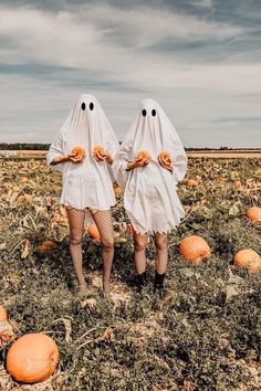 two women dressed in ghost costumes standing in a field with pumpkins