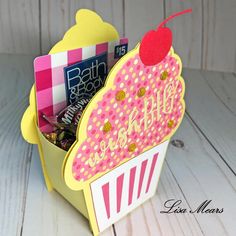 a pink and yellow cupcake shaped card holder with candy in it's side