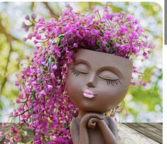 a ceramic figurine with purple flowers on her head and eyes closed, sitting in front of a tree