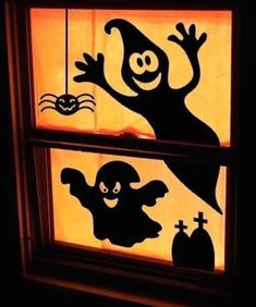 two windows with halloween decorations on them and one window is lit up in the dark