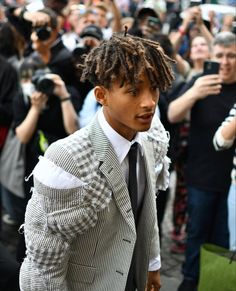 a young man with dreadlocks walking in front of a large group of people