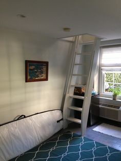 a room with a bed, ladder and window in the corner next to a blue rug