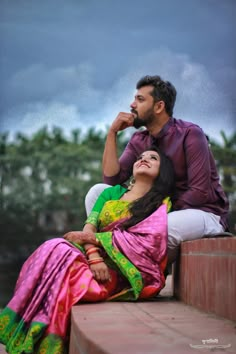 a man and woman sitting next to each other on the ground with trees in the background