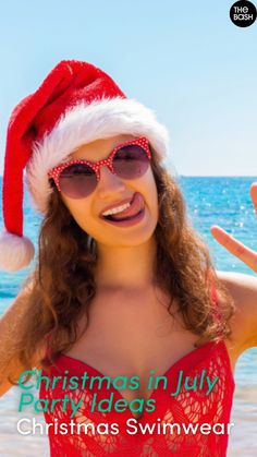 a woman wearing sunglasses and a santa hat on the beach with her hand up in the air