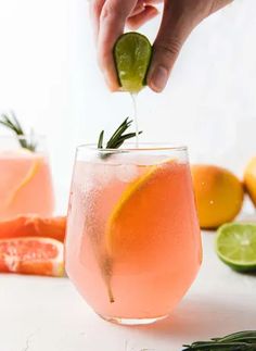 a person is squeezing a lime into a glass filled with pink lemonade and rosemary