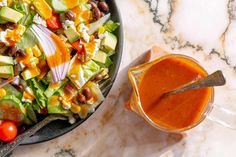 a salad with dressing in a bowl on a marble counter top next to a spoon