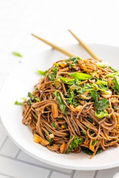 noodles with broccoli and carrots on a white plate next to chopsticks