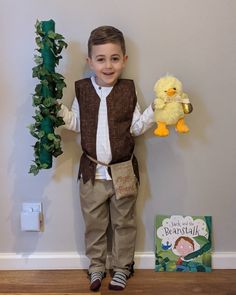 a young boy holding a stuffed animal next to a book and a toy duck on the floor