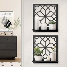 two black shelves with plants and candles on them in front of a wall mounted poster