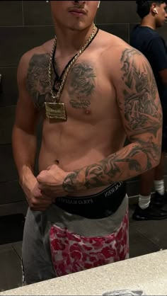 a man with tattoos on his arm and chest standing in front of a counter top