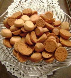 a glass bowl filled with small cookies on top of a wooden table next to a lace doily